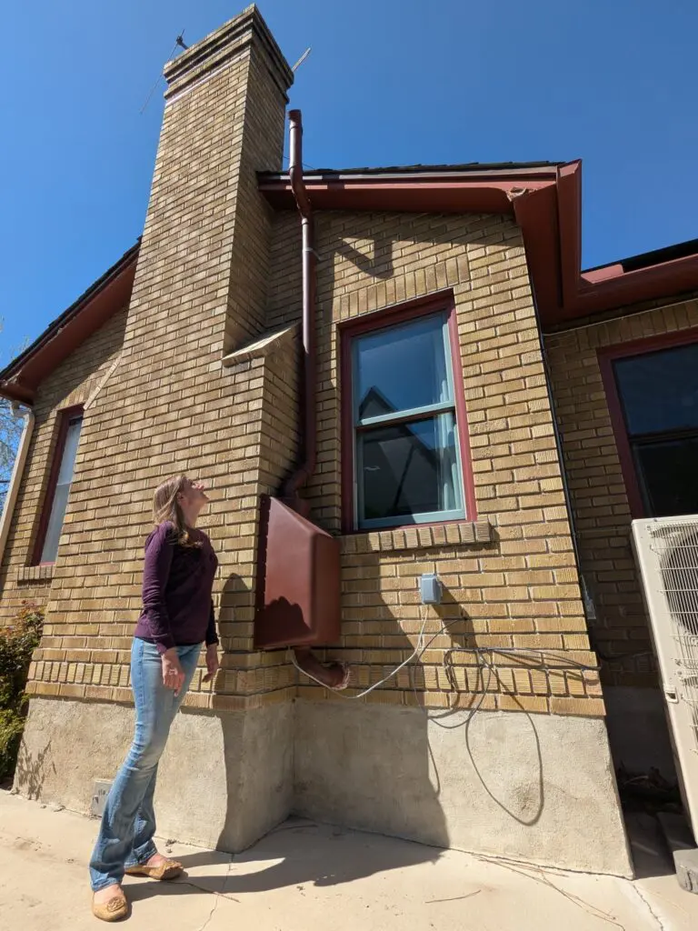 Reno resident Heather Gage looks up at the full radon mitigation system installed outside her Reno home. The red box contains a fan that pumps radon-rich air through the pipes and up through the top exhaust vent. Photo Mike Escobar / Sierra Nevada Ally
