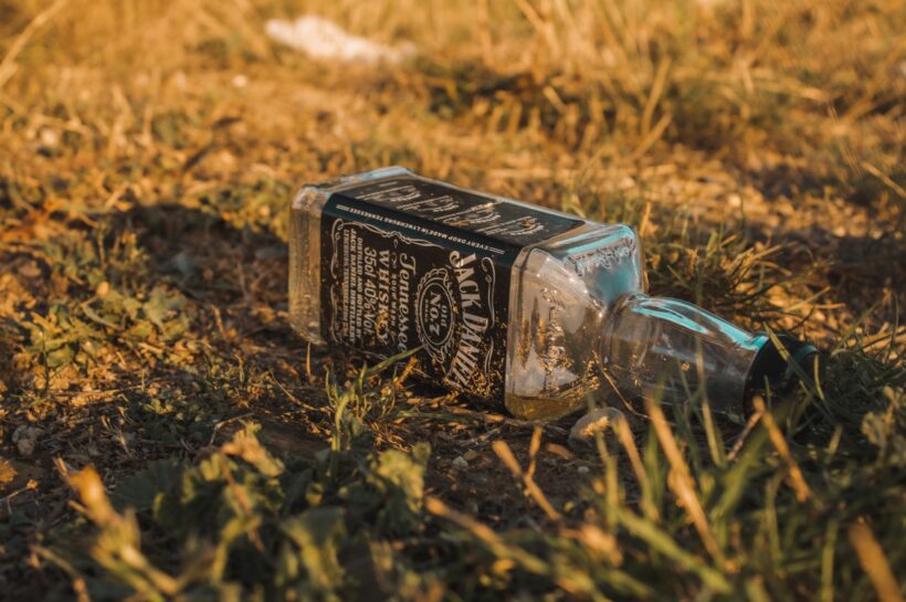 Close-up of an empty whiskey bottle lying on grass, evoking an earthy and gritty mood. Photo by Emre Yaşar from Pexels.