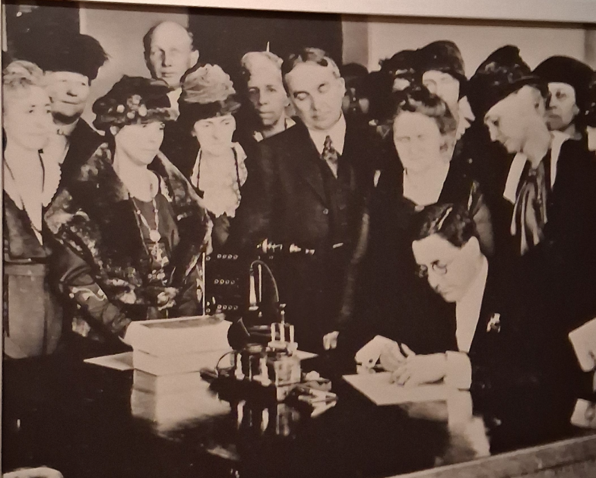 Photo of a historical photograph exhibit showing Nevada Governor Emmet D. Boyle signing the resolution ratifying the 19th Amendment (granting women the right to vote) in Carson City, Nevada, on February 7, 1920. Courtesy of Johanna Ruiz Lopez.